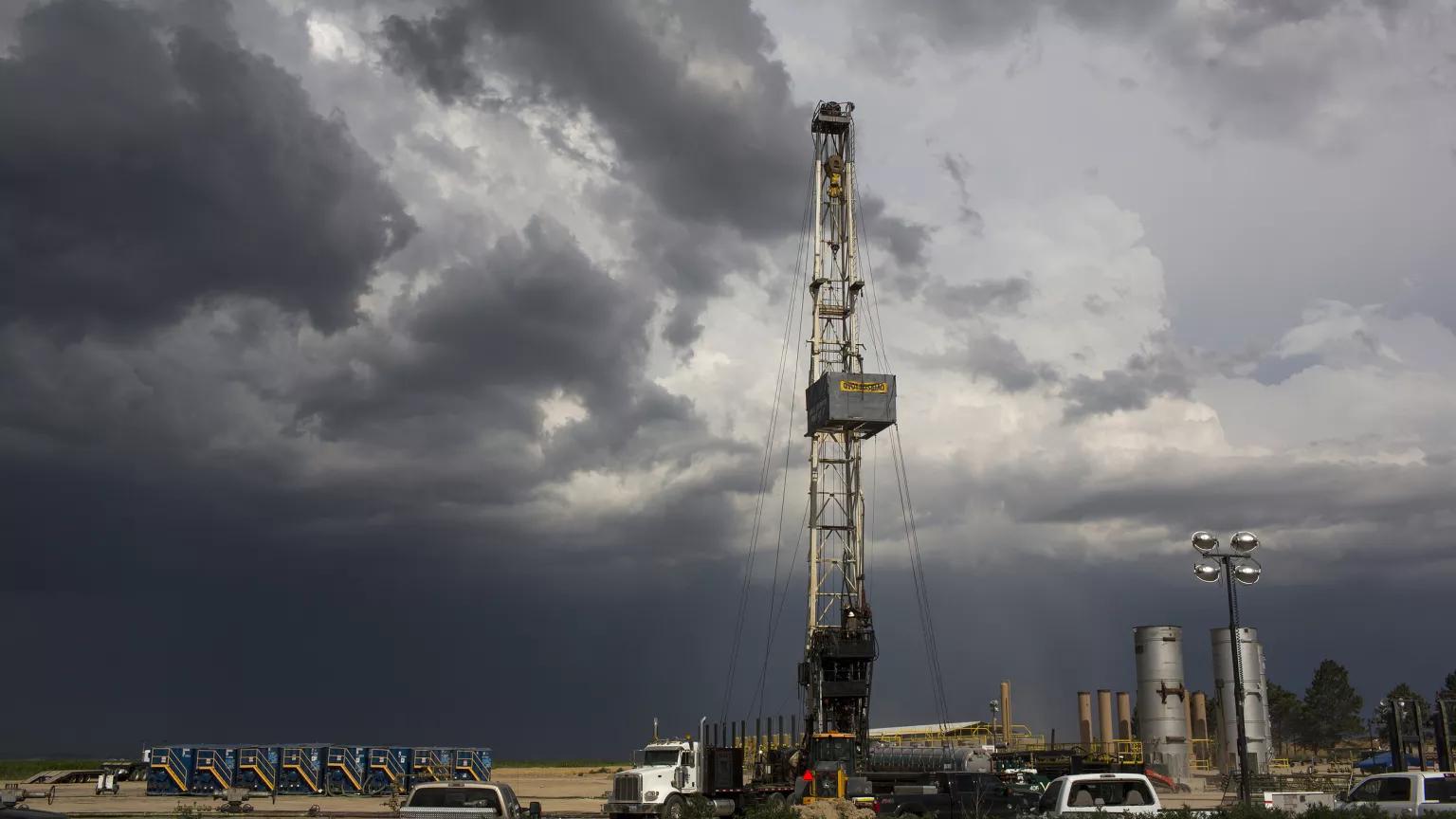 A rig rises from a field with dark gray clouds on the horizon