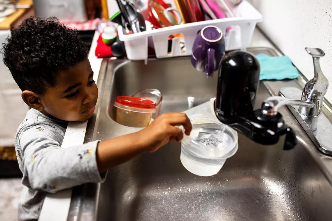 A child fills a cup of water from a kitchen faucet with a filter attached to it