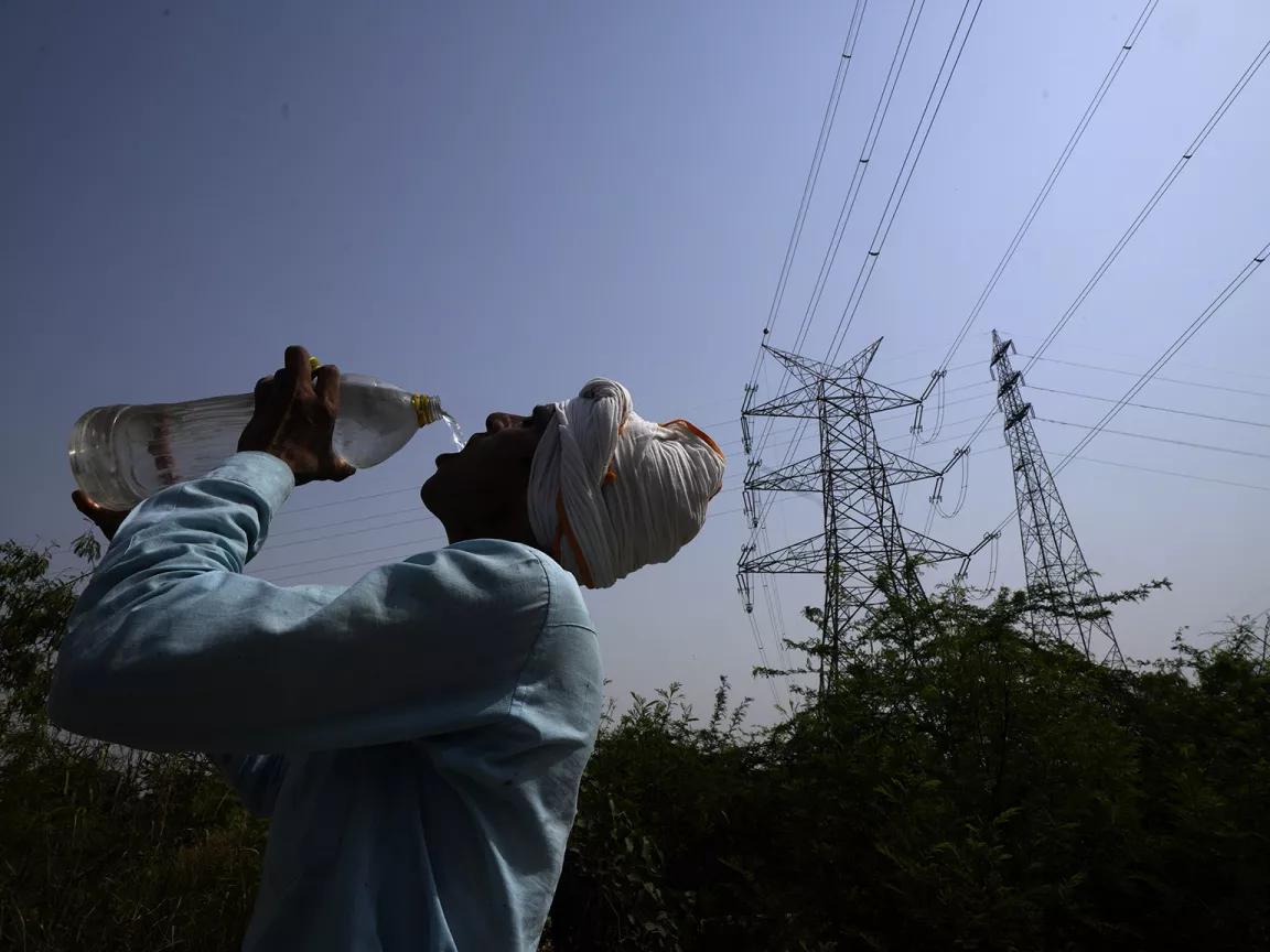 A worker drinking water from a bottle with power lines in the background.