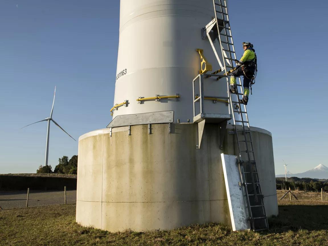 A worker climbing a ladder on the base of a wind turbine at Aurora Wind Farm in Chile