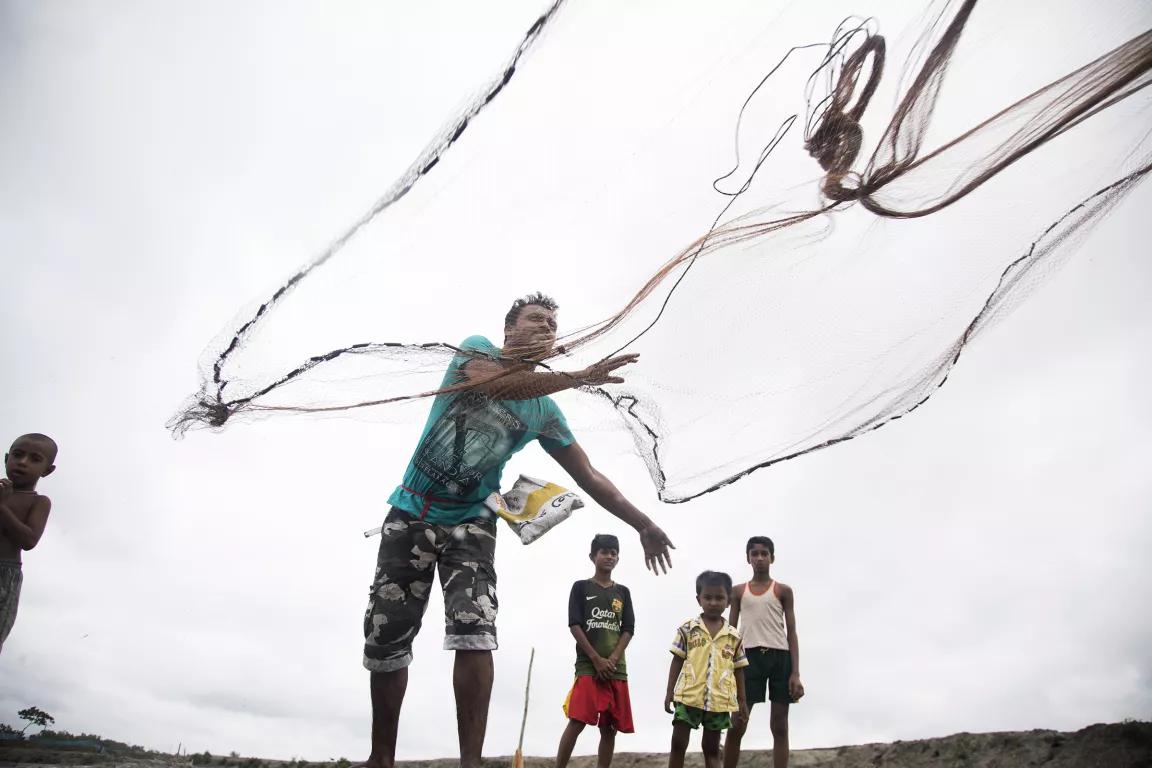 A man throws out a large fishing net while three children watch from behind him