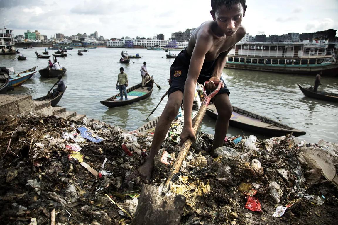 A young boy on the bank of a river sifts through trash and debris