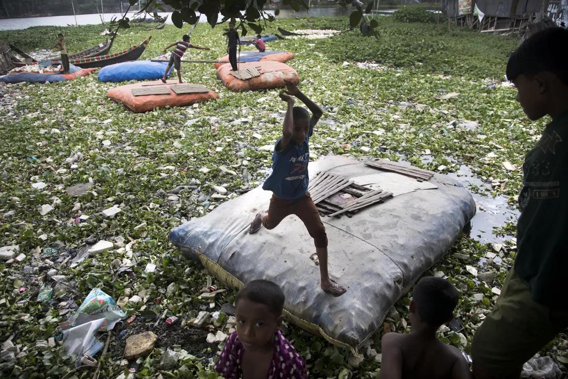 Children play on floating rafts surrounded by trash and debris