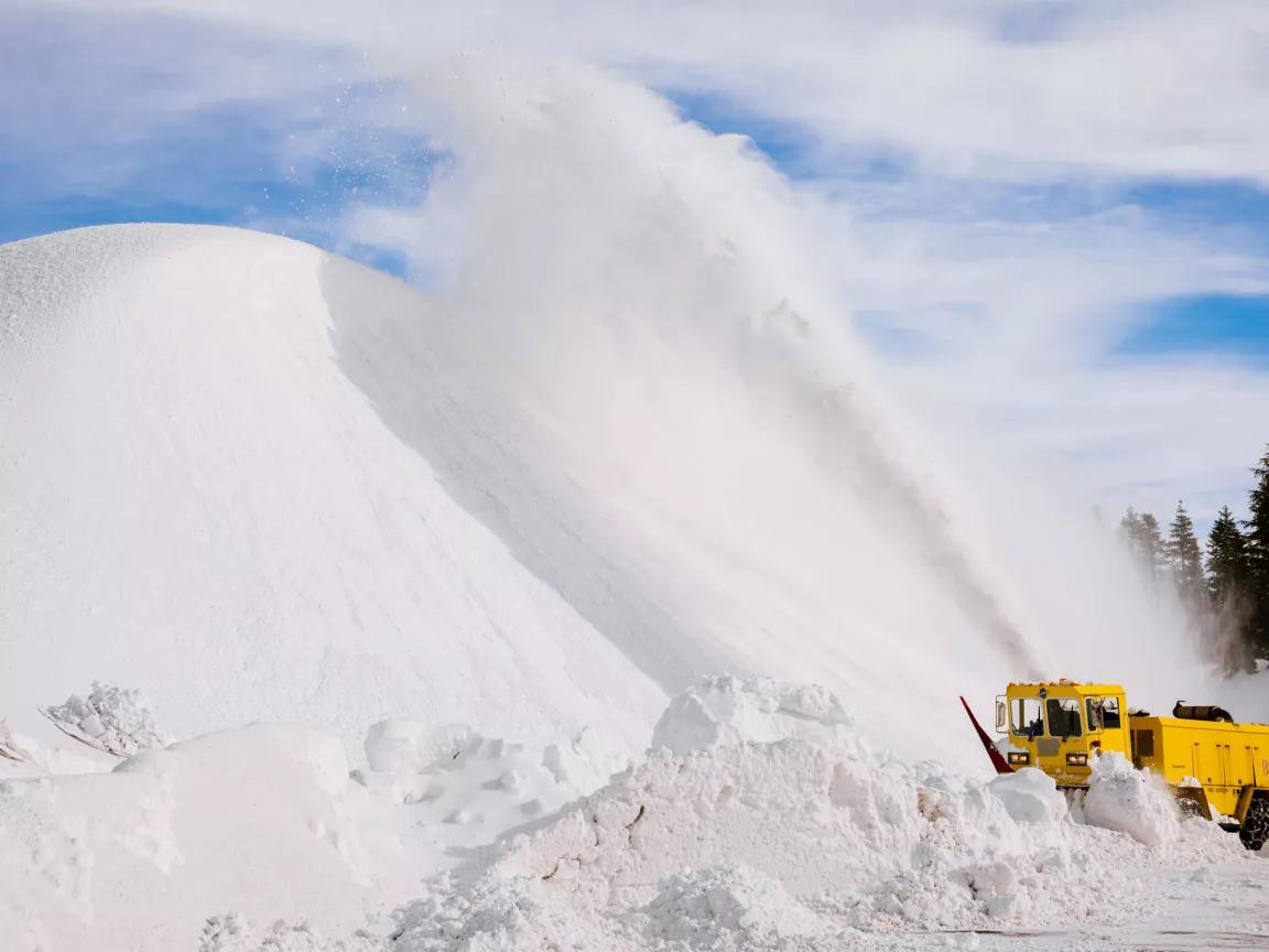 A heavy-duty truck blows snow into an enormous mound in a parking lot