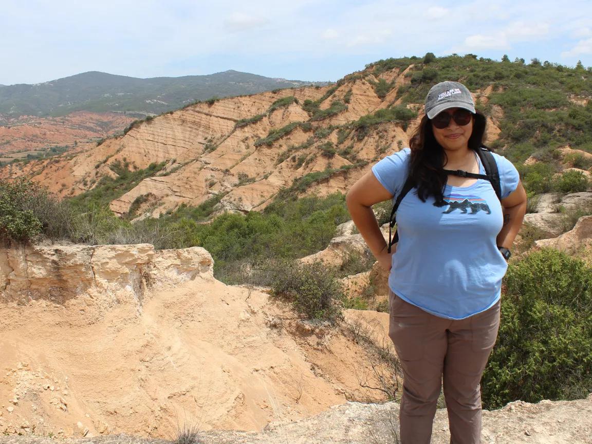 Elybeth Alcantar standing on a ridge with an expanse of rugged, dry terrain behind her