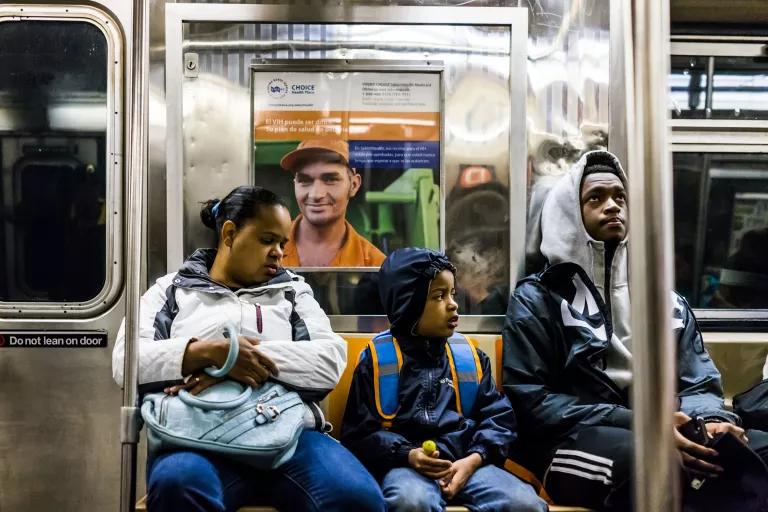 A woman, child, and young man seated in a subway car