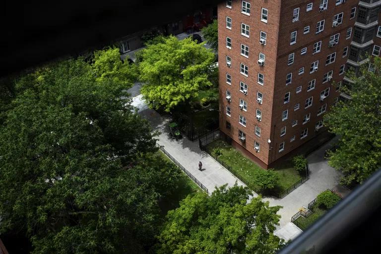 A view from above of a tall brick apartment building and paved, tree-lined pathways below