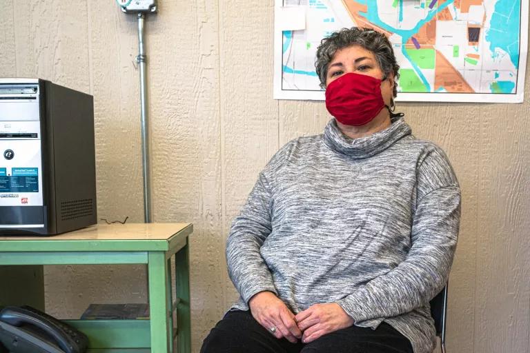 A woman wearing a red face mask sits in a chair in front of a map hanging on an office wall