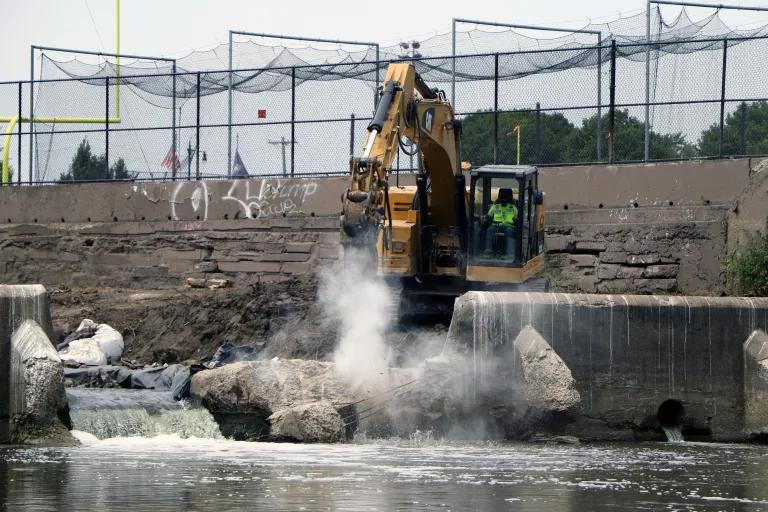 A large crane moves chunks of concrete from a riverbed