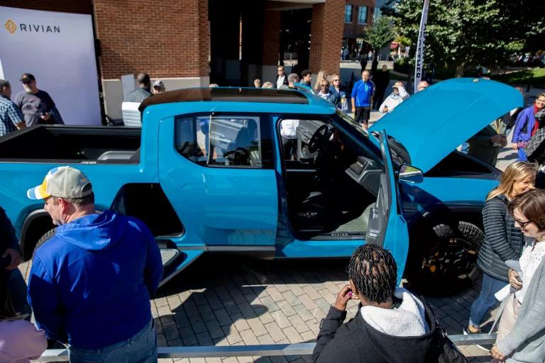 People surround a bright blue pickup truck with its hood and doors open