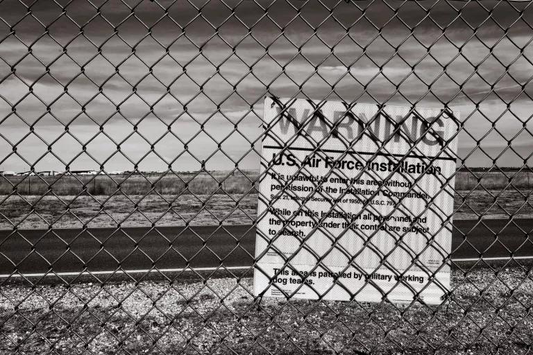 A sign hanging on a chainlink fence reads in part "Warning: U.S. Air Force Installation"