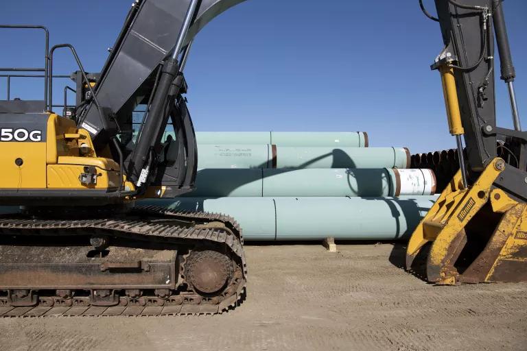 A stack of large green-colored pipeline segments sits next to construction equipment.