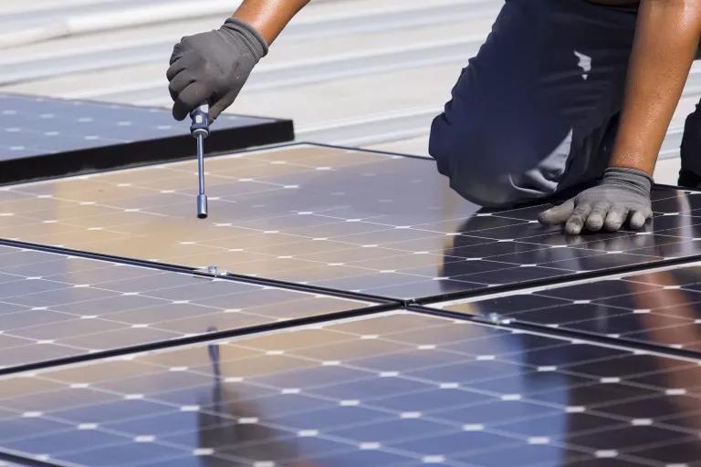 A person uses hand tools while installing a solar panel on a roof