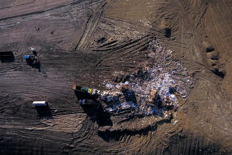 An aerial view a landfill, with a trash haulers moving a large pile of debris surrounded by barren land