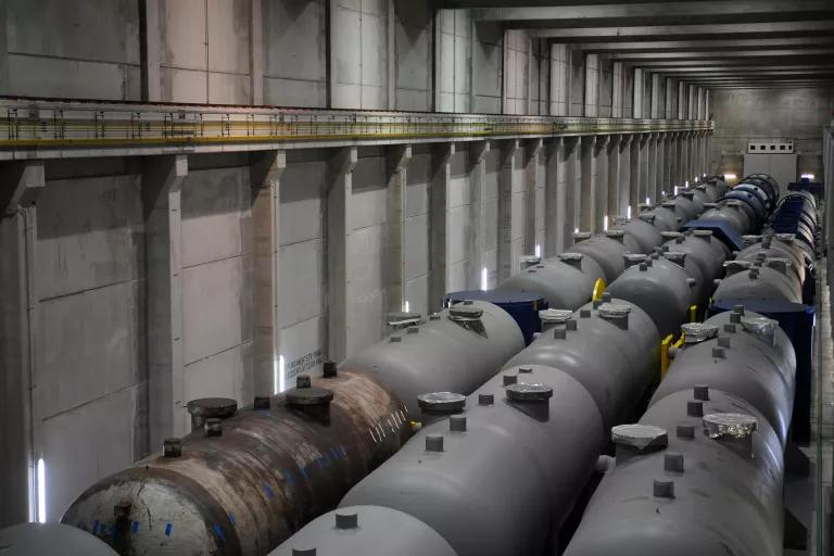 Three long rows of gray tanks are lined up inside an enclosed building