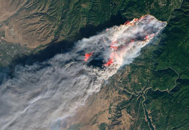 An satellite view of a wildfire and smoke in a forested area