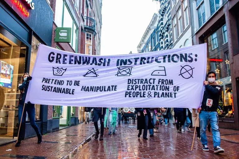 A group of protesters hold a large banner that mimics a laundry instruction tag and reads "Greenwash Instructions"