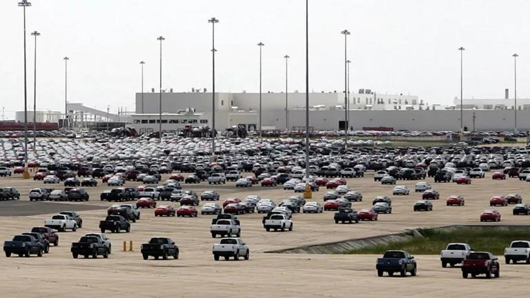 A vast parking lot full of cars with large buildings in the background