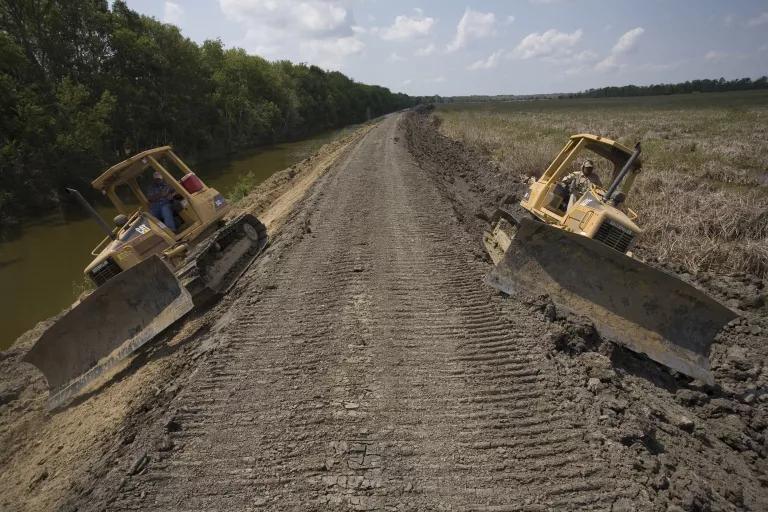 Two bulldozers sit on either side of a long dirt roadway