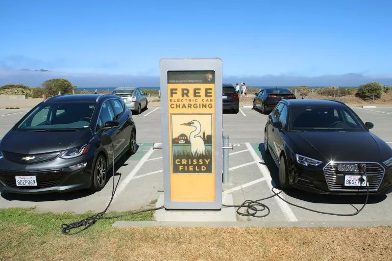 Two cars sit plugged in on either side of an electric charging station