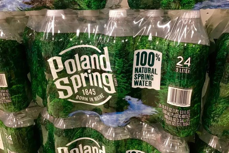 A case of bottled water with the Poland Spring logo in white writing on a background of green trees