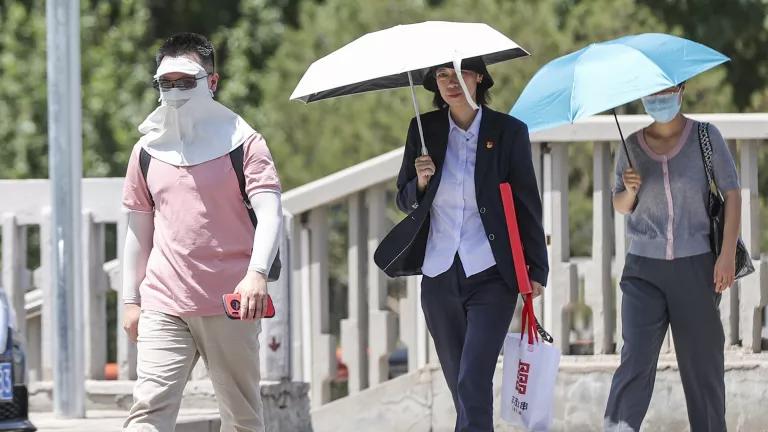 Pedestrians use umbrellas and protective clothing for shade in Beijing, China