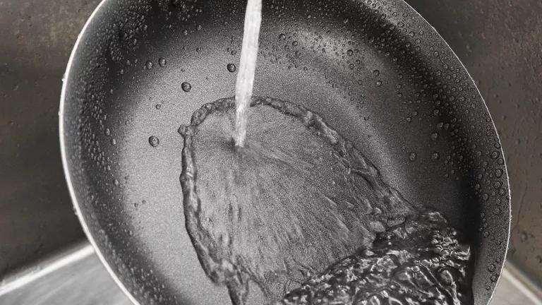 A nonstick frying pan being rinsed in a kitchen sink.