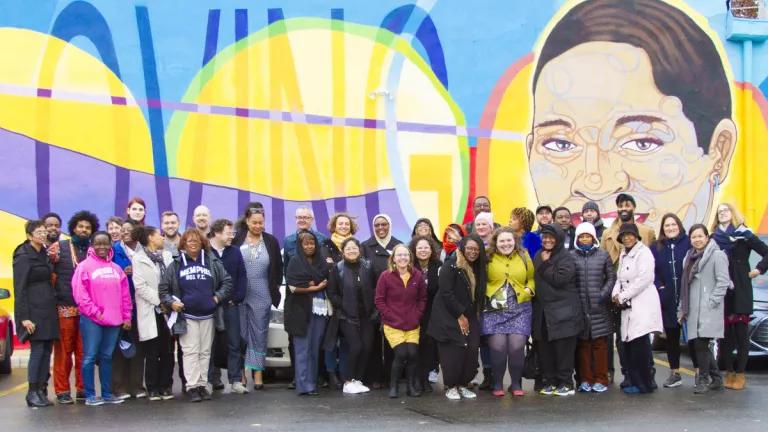 A group of people in front of a mural showing a person's face on the right