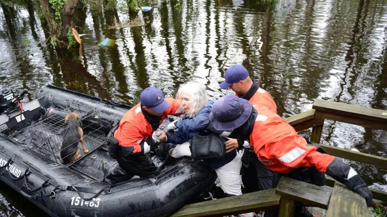 Three rescue workers help an elderly woman move from a flooded staircase into an inflatable raft