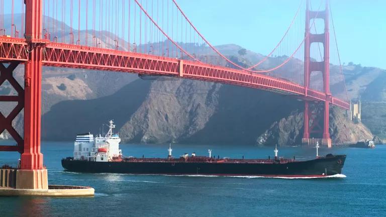 A red bridge with a big oil tanker in the water passing beneath it