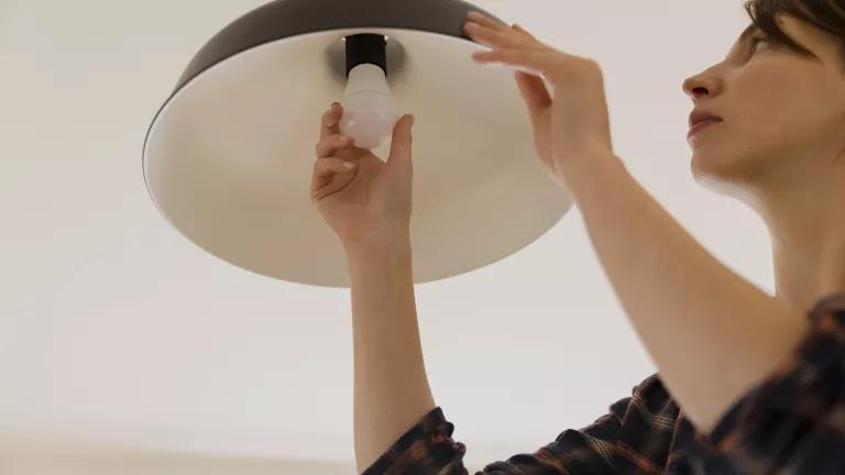 A woman changes the lightbulb in a fixture mounted on a ceiling