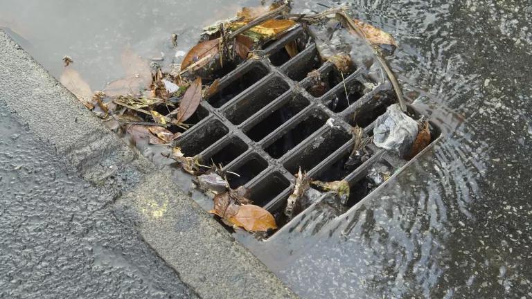 Water and debris rushes into a sewer grate on a city street