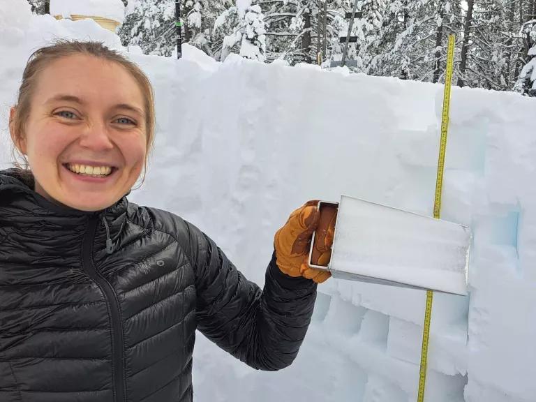 A woman holds a rectangular sample of snow extracted from the middle of snowpack as tall as she is