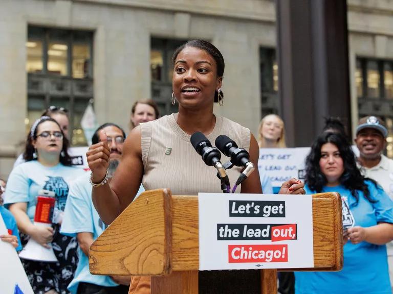 Chakena D. Perry stands at an lectern bearing a sign that reads "Let's get the lead out, Chicago"