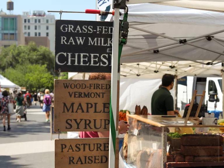 Wooden signs at a city farmers market advertise grass-fed raw milk cheese and Vermont maple syrup