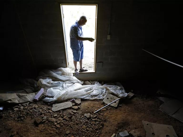 A man stands in the doorway of a darkened room where dirt and debris sit on the floor
