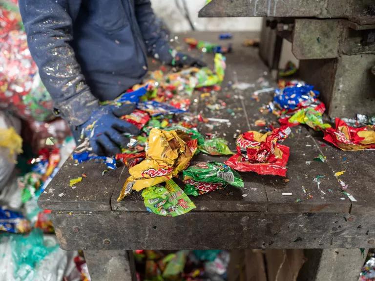 A person stands over a wooden table where a pile of plastic wrappers and trash are sorted