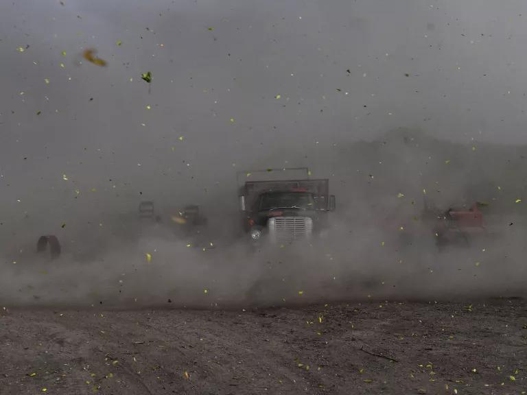A cloud of dust and debris obscure trucks and heavy equipment in the background.