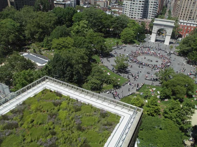 An aerial view overlooking a garden on the roof of a tall building with tree-lined city blocks below it