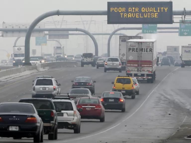 Cars drive on a highway below an electronic traffic sign that reads "Poor air quality; travel wise"