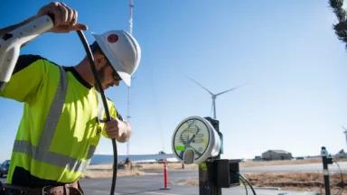 A worker installing an electric vehicle charger with wind turbines in the background