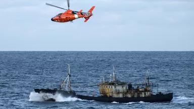 A U.S. Coast Guard helicopter hovers over a fishing vessel in the Northern Pacific Ocean.