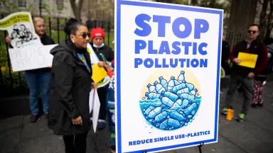 A sign that read "stop plastic pollution" with an illustration of a pile of single use plastic bottles being displayed at a rally