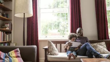 A man and small child look at a book together on a couch in a home living room