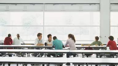Students sit at long tables in a school cafeteria