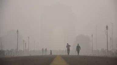 Two people walk through a thick haze on a city street