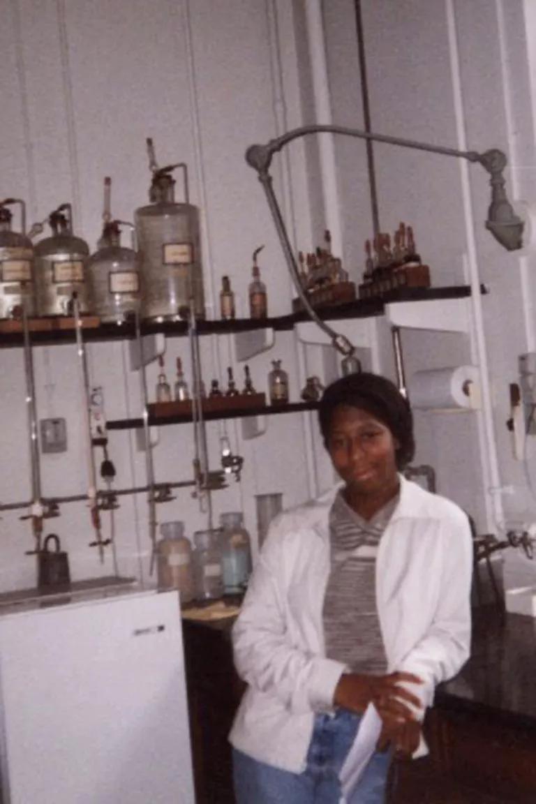 A woman stands in front of shelves holding chemistry lab equipment