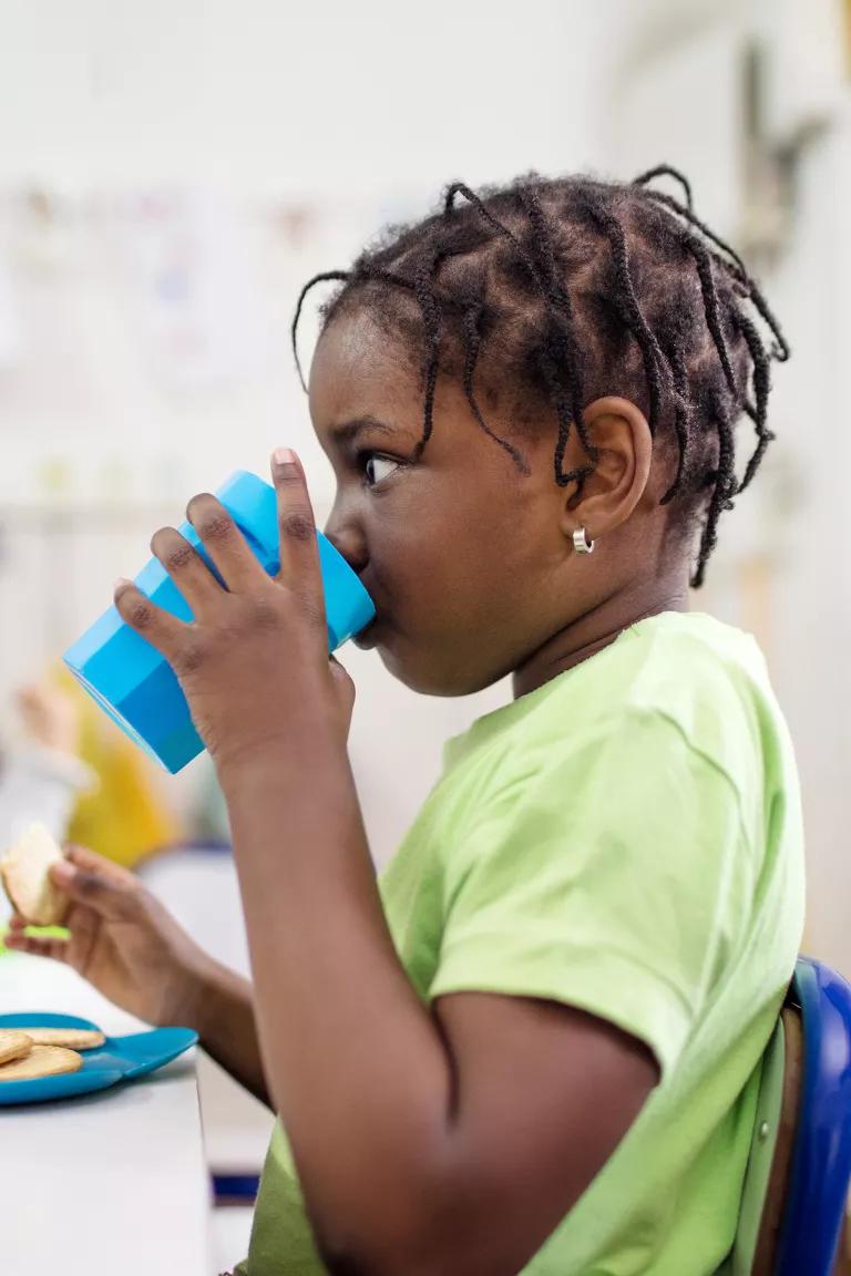A child sitting at a school table drinks from a cup