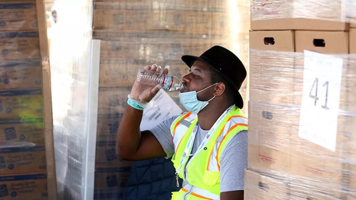 L.A. County Parks and Recreation worker Lionel Taplin drinking water while helping to deliver boxes of food to low-income families under the hot sun in Saybrook Park, Montebello, California