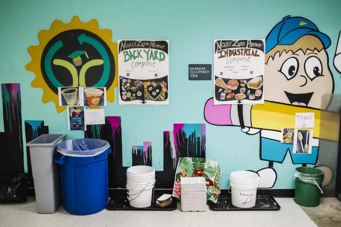 A wall in a school cafeteria with bins and signs that read Backyard compost, Industrial compost, Waste and Trash